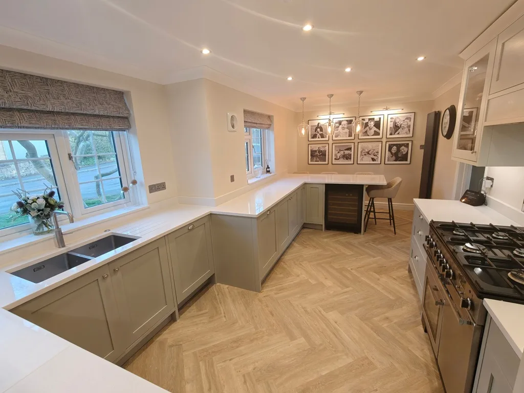 Beautiful modern sage green kitchen renovation by LTK Services - featuring sage green cabinets, white quartz countertops, herringbone parquet flooring, pendant lighting, and gallery wall of framed artwork